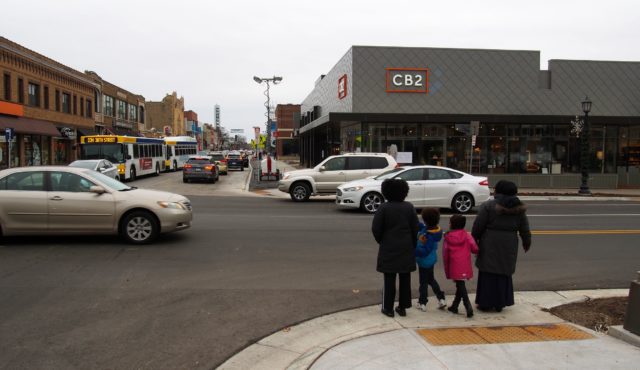 Two pairs of black women and children wait to cross a busy street in Minneapolis, MN