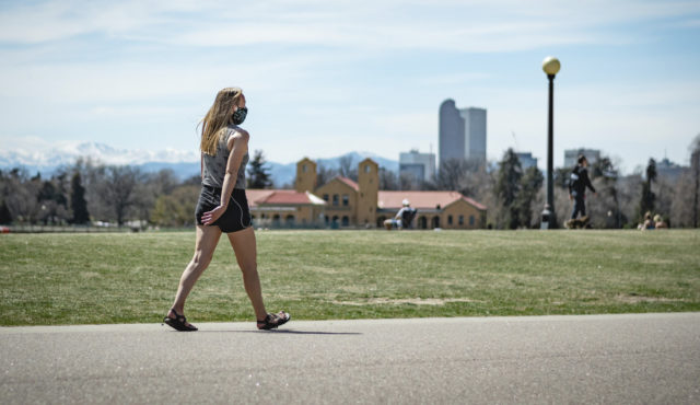 Woman walking by Denver skyline wearing face mask