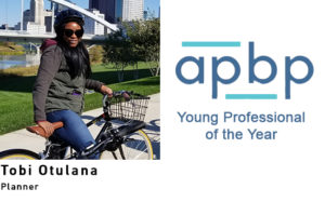 Tobi Otulana is facing the camera, straddling a bike in front of the Columbus skyline