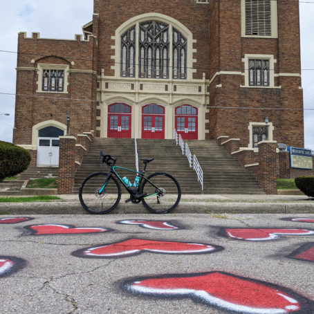 Photo of a bike in front of an old church. Hearts are spraypainted on the asphalt.