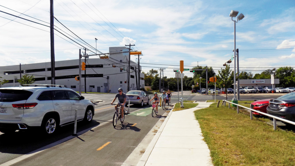 Families with children use a dedicated bike lane on a busy street in Austin, Texas.