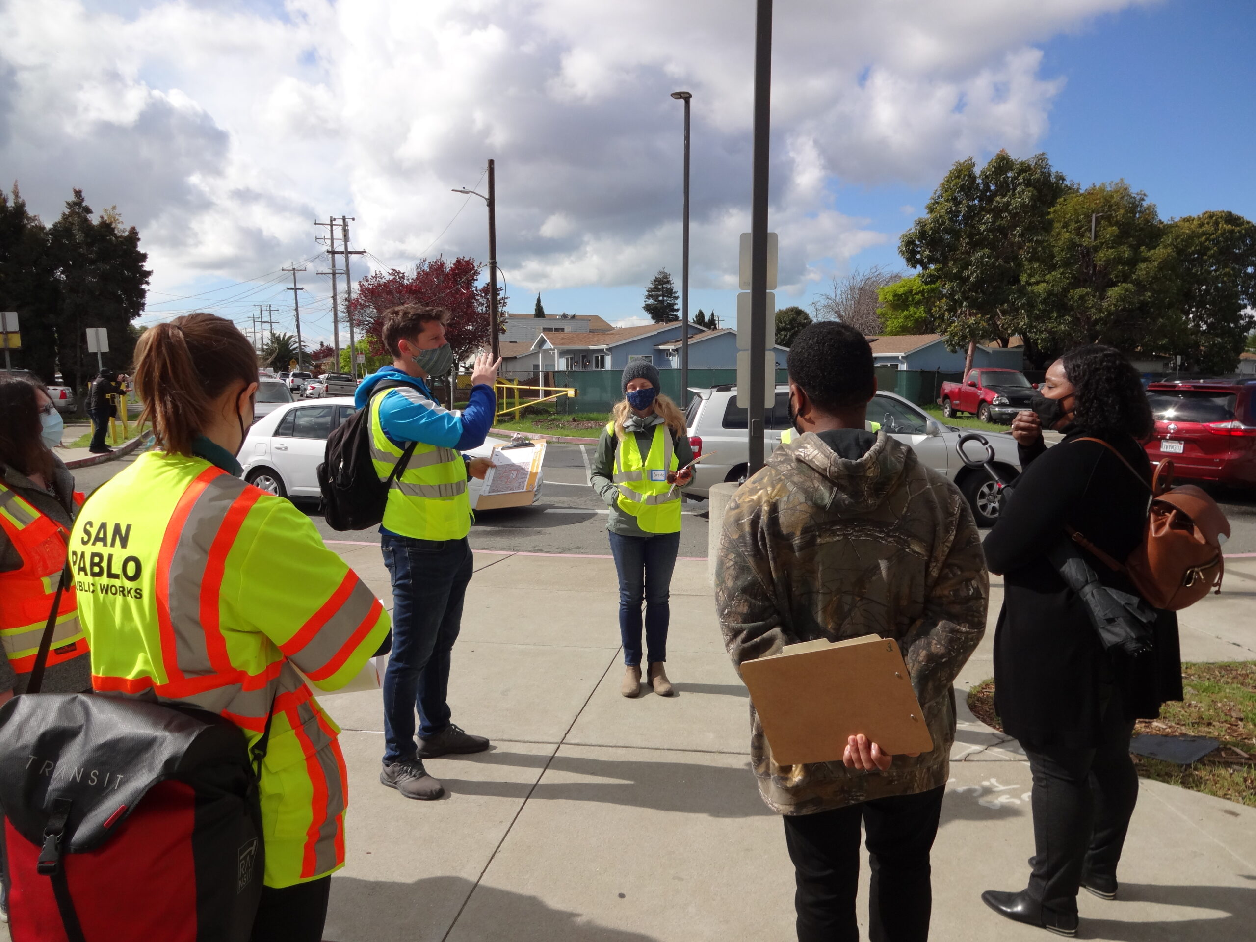 A group of people, some in San Pablo Public Works safety vests, stand on a sidewalk during a walk audit of a school for the San Pablo SR2S Plan.