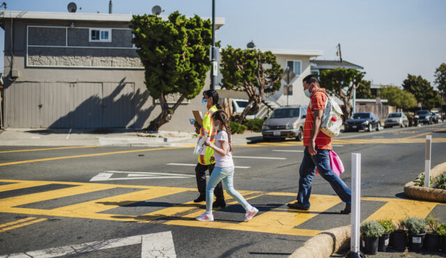 A father and daughter cross at a pedestrian crossing.