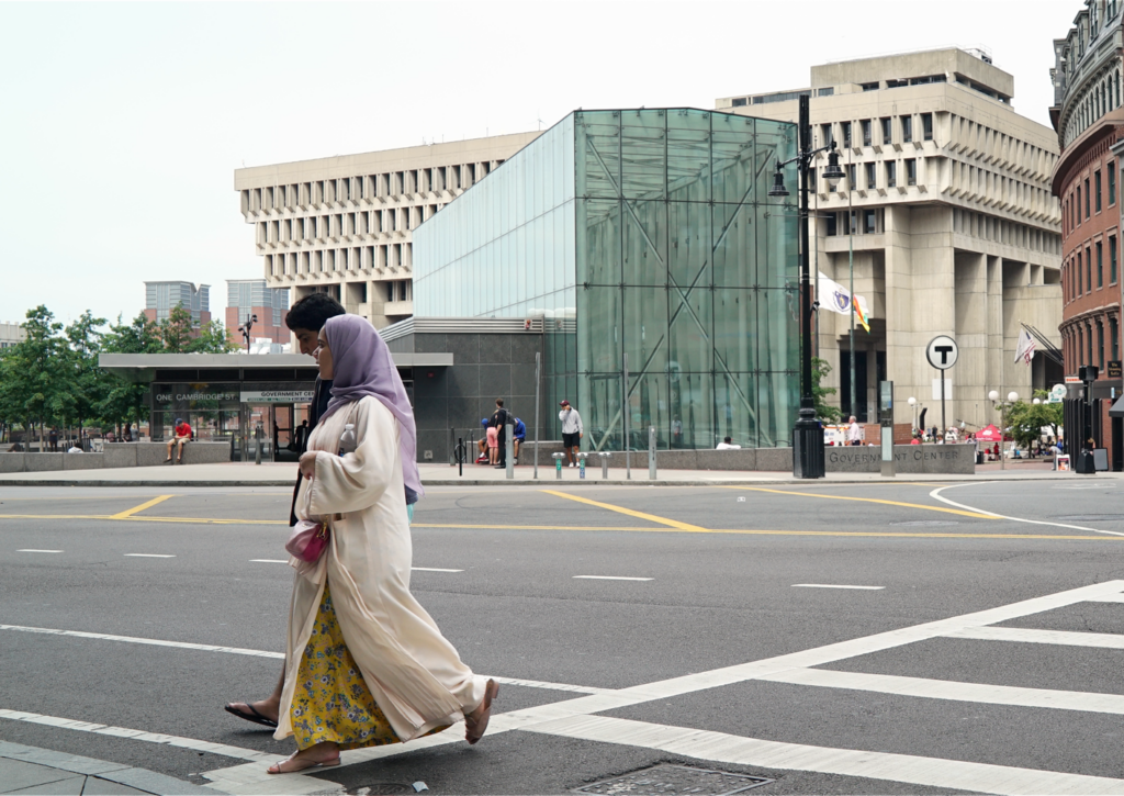 Two pedestrians, one wearing a hijab, cross a street in an urban area.