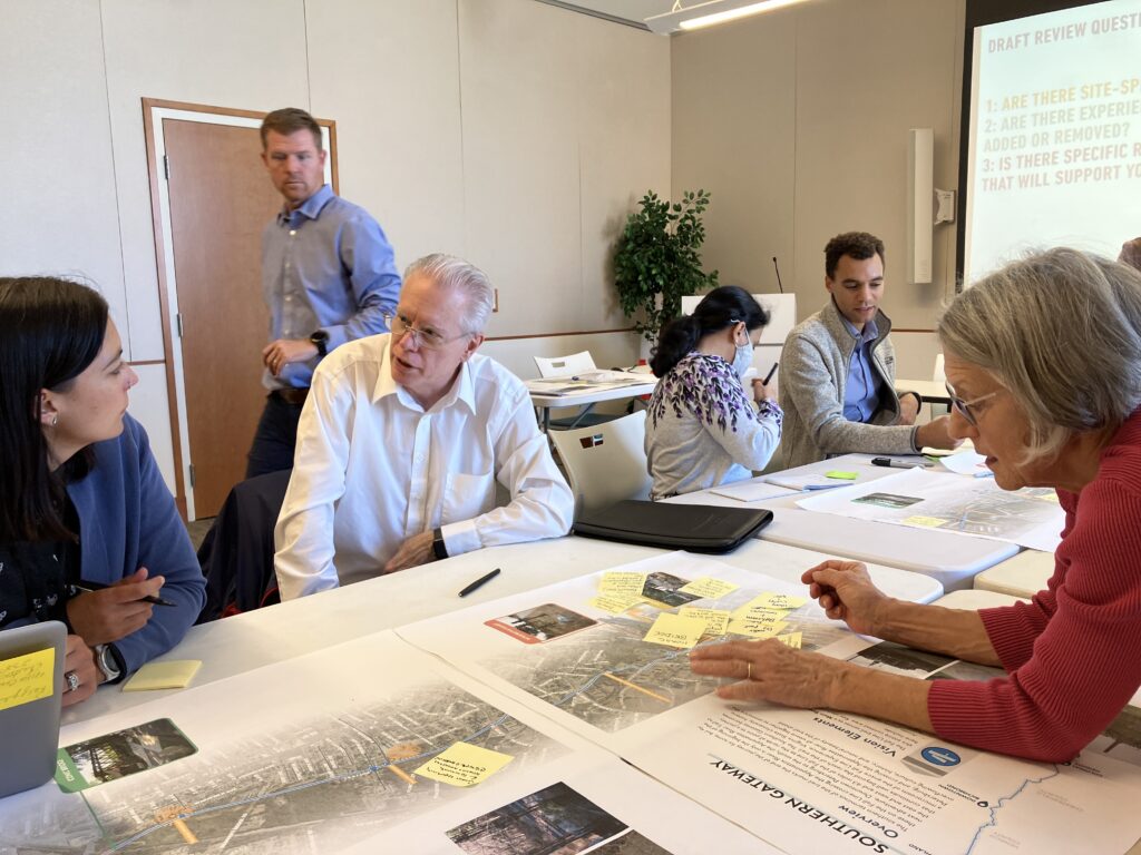 People seated around a table review a trail map covered in sticky notes, discussing ideas during a planning charrette.